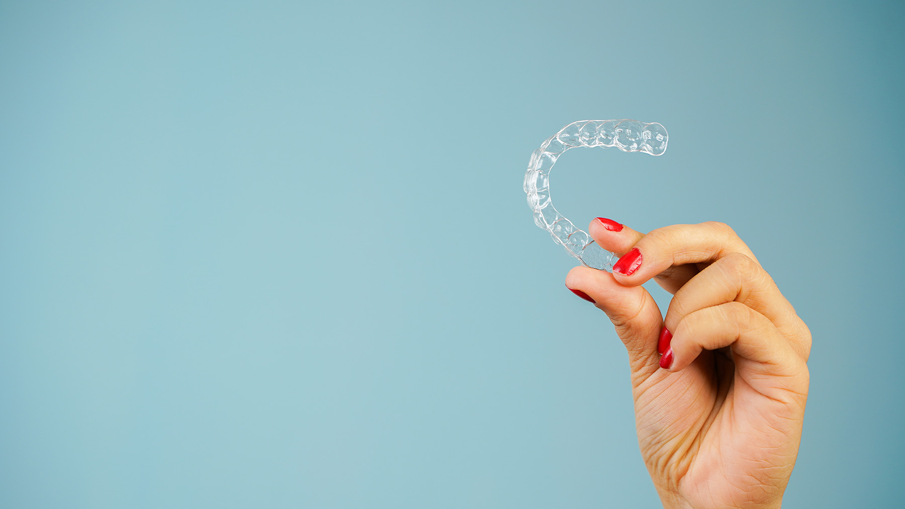 The image shows a hand holding up a clear plastic dental retainer against a blue background.