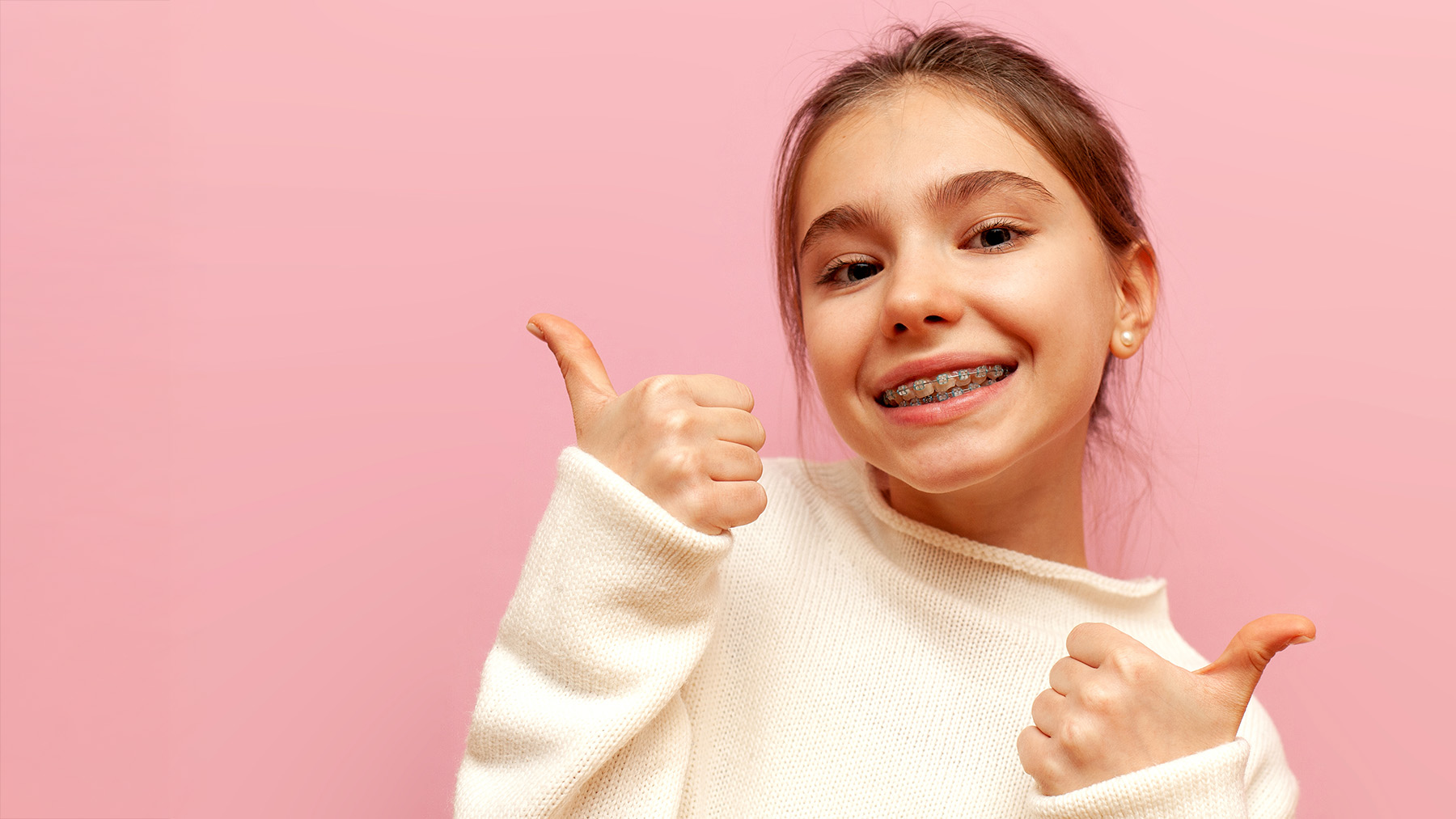 A young girl with thumbs up gesture against pink background.