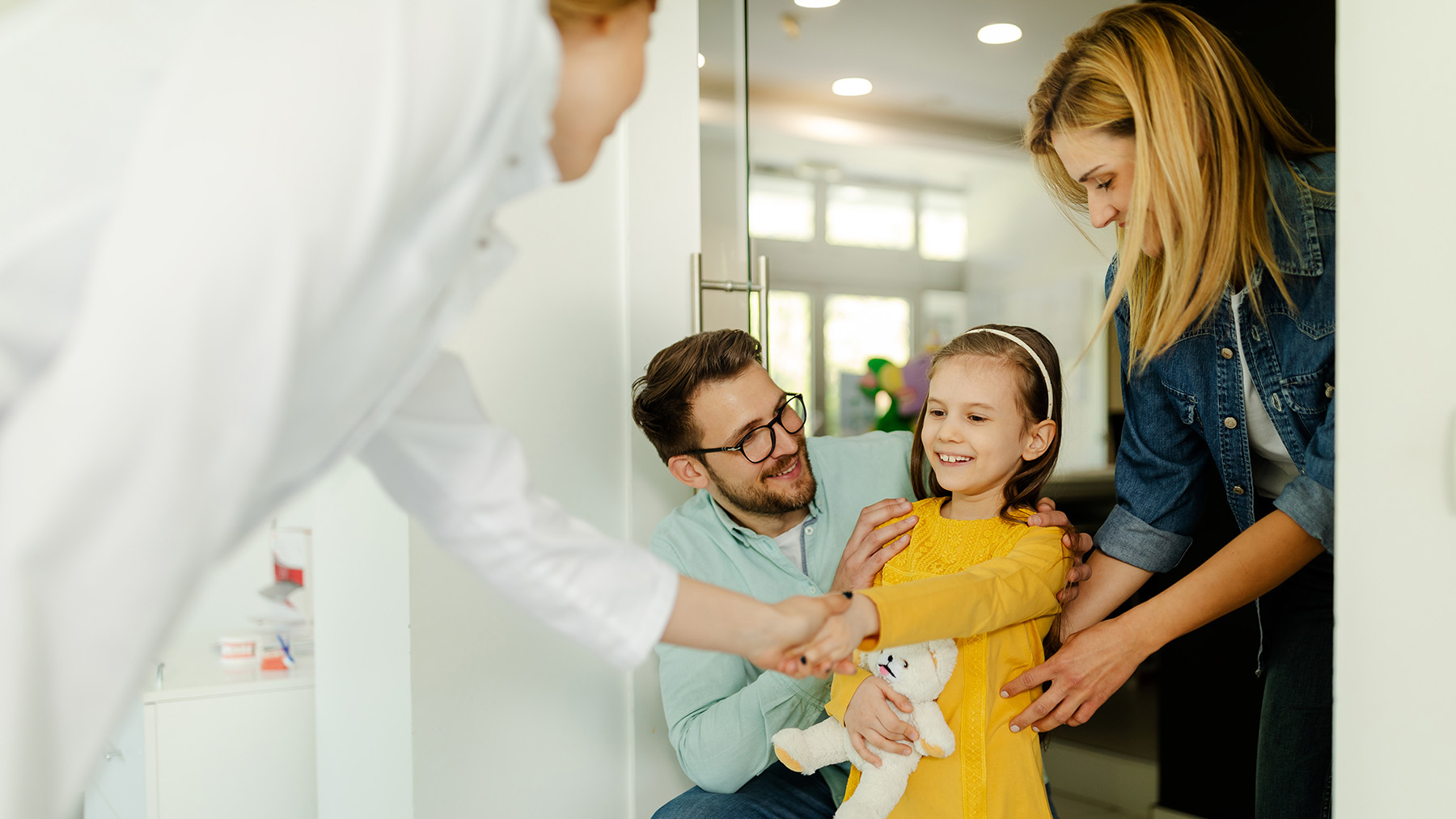 A family, including adults and a child, gathered around a young girl who is sitting on a man s lap, all looking at something off-camera with smiles on their faces.