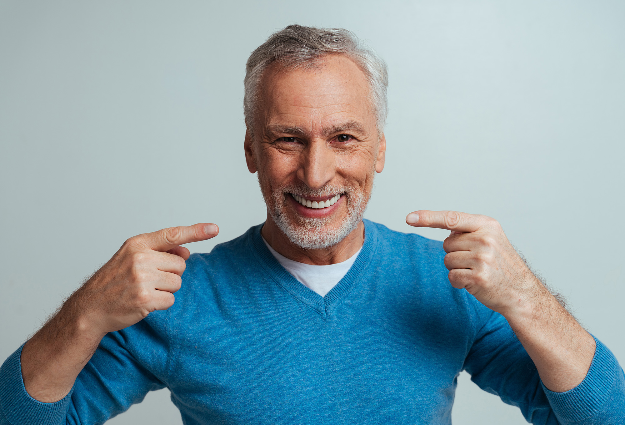 Man pointing at his finger with both hands, smiling broadly against white background.