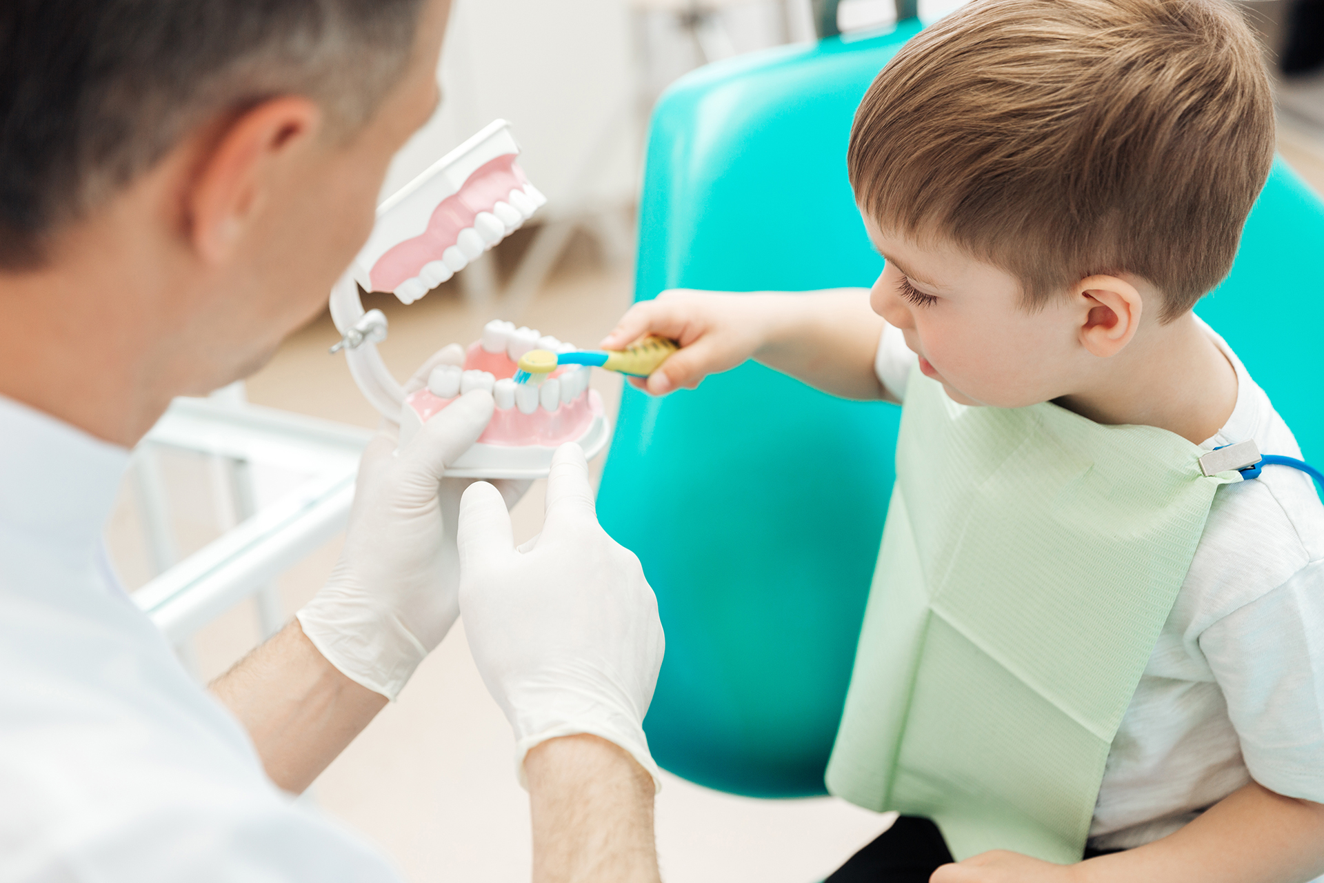 A young boy is sitting in a dental chair, receiving dental care from a dentist, with a toothbrush being used on his teeth.