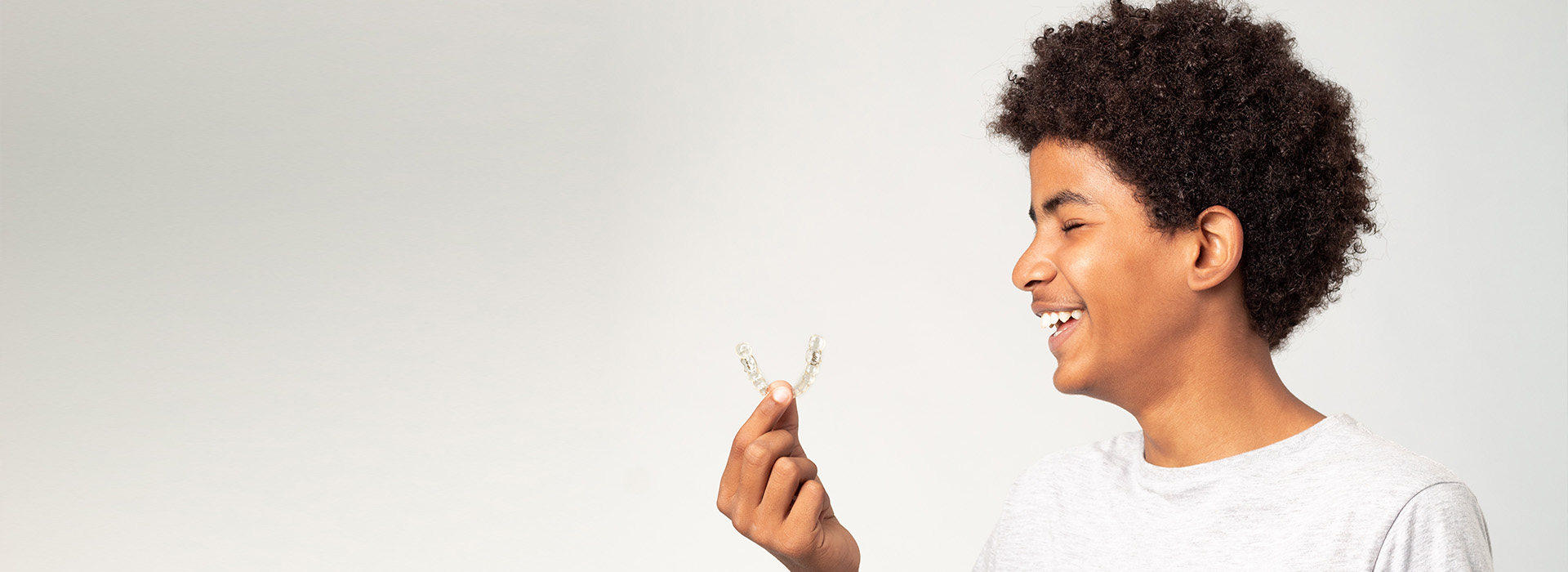 A young man with curly hair holds up a small object with both hands, smiling at the camera.