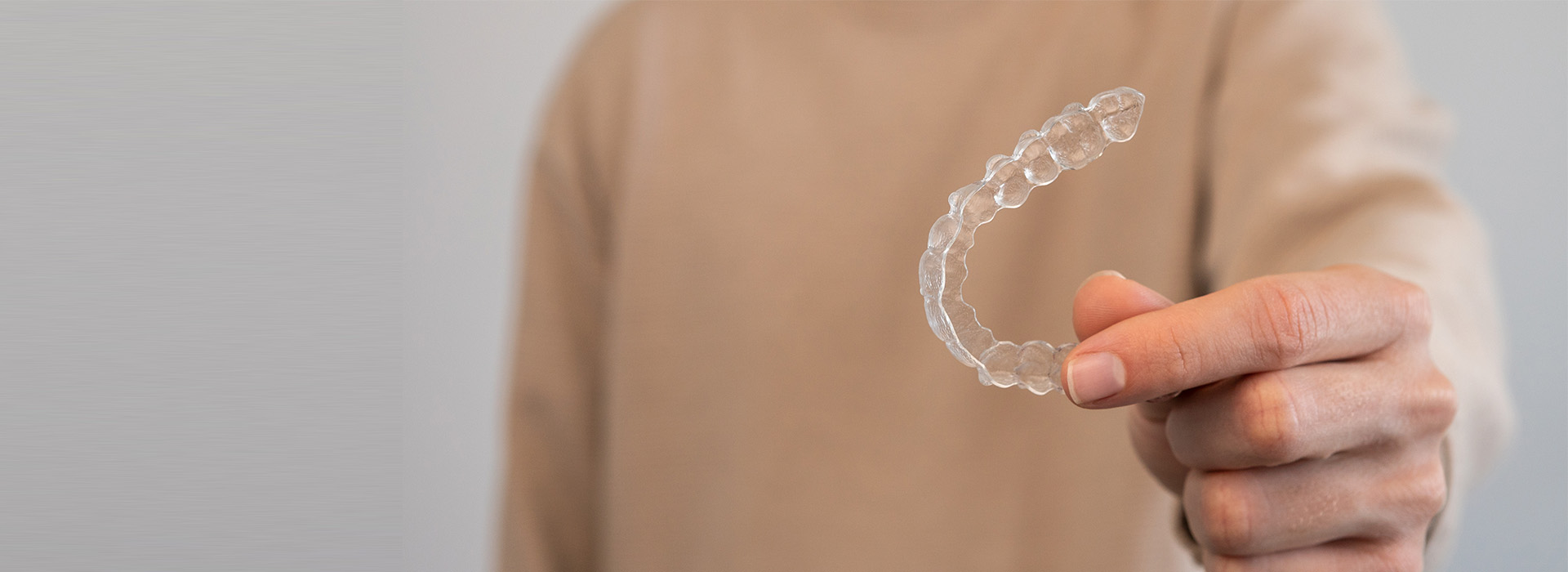 The image shows a human hand holding a single clear plastic ring against a blurred background.