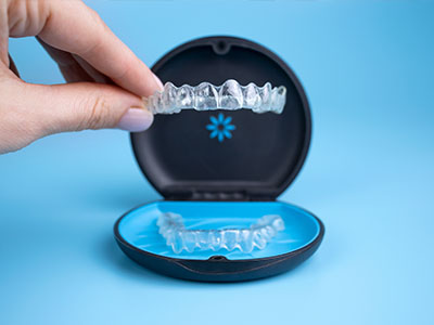 The image shows a hand holding an open dental impression tray containing transparent plastic aligners, with a focus on the aligners being placed into the tray.